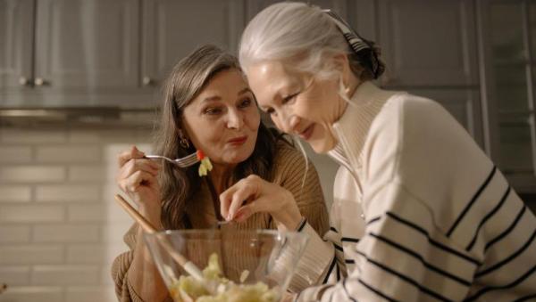 Dos amigas mayores preparando y disfrutando una ensalada juntas en la cocina