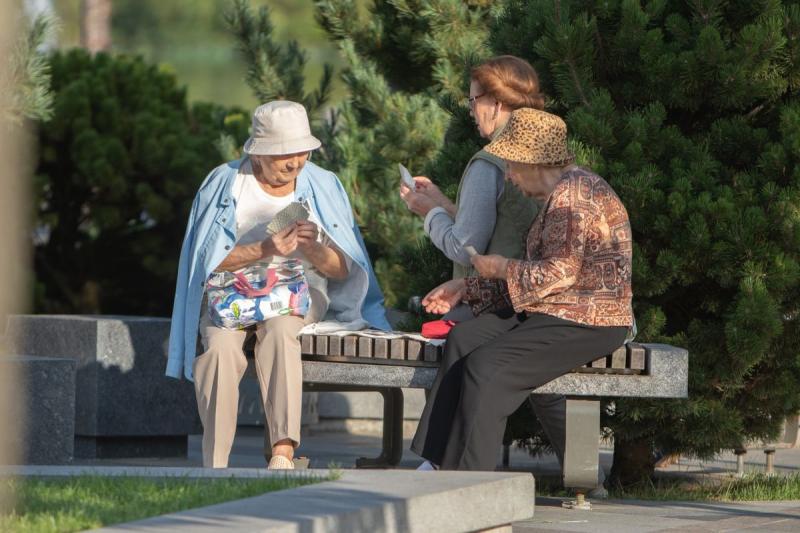 Tres amigas mayores jugando a las cartas juntas en un banco del parque