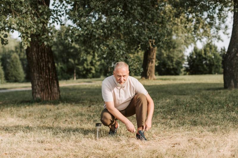 Hombre mayor atándose los cordones de las zapatillas al aire libre antes de caminar
