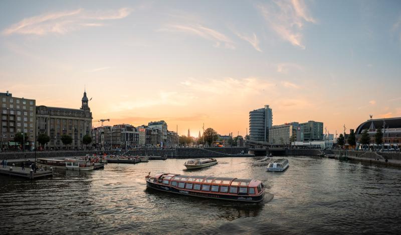 Barcos turísticos navegando por los canales de Ámsterdam al atardecer