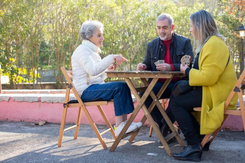 Tres personas mayores jugando a las cartas en una mesa al aire libre