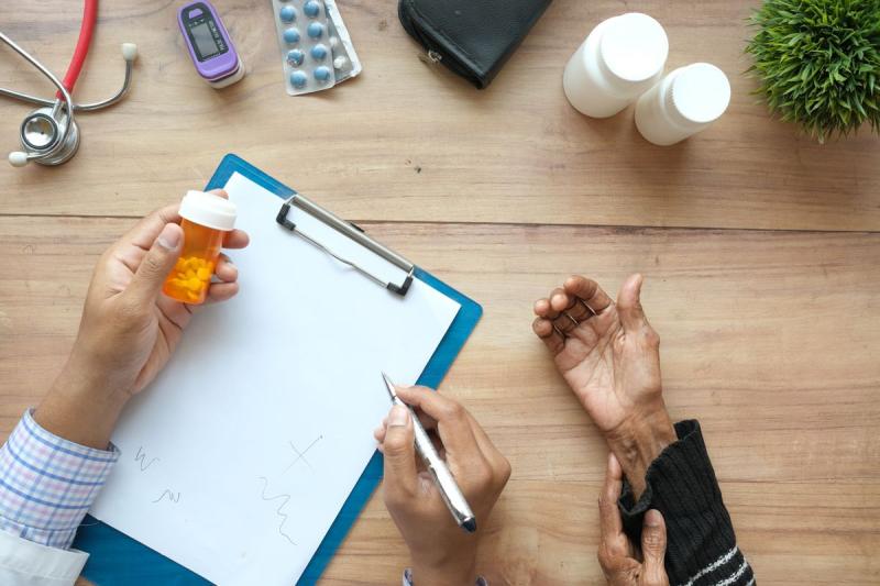 Manos de un médico y de un paciente mayor sobre una mesa con recetas y medicación