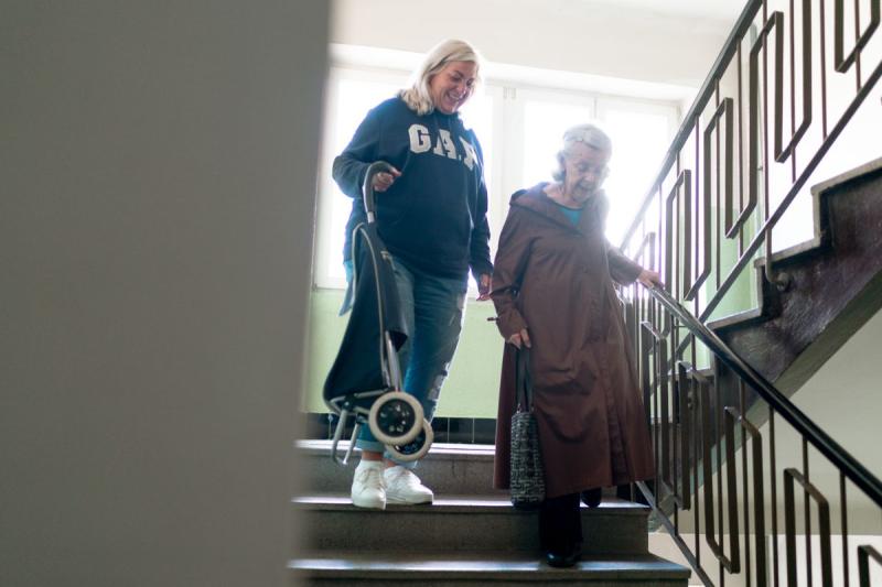 Mujer mayor bajando las escaleras sujeta al pasamanos acompañada