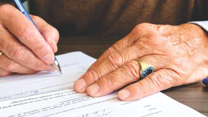 Manos de una persona mayor firmando un documento legal