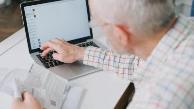 Hombre mayor gestionando sus finanzas online con documentos y portátil