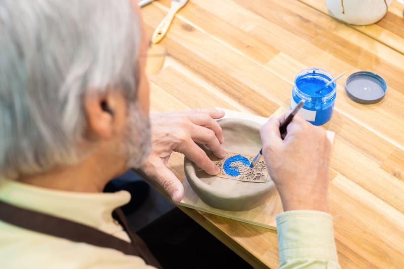 Hombre mayor pintando un cuenco de cerámica con pincel