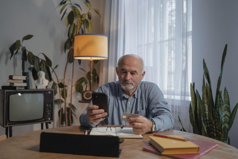 Hombre mayor mirando con cautela el móvil y una tarjeta bancaria