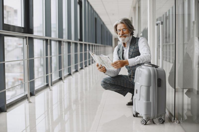 Hombre mayor con maleta leyendo un mapa en un pasillo de aeropuerto