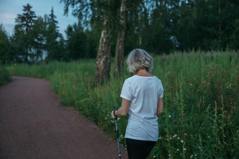 Mujer mayor caminando con bastones nórdicos por un sendero al aire libre