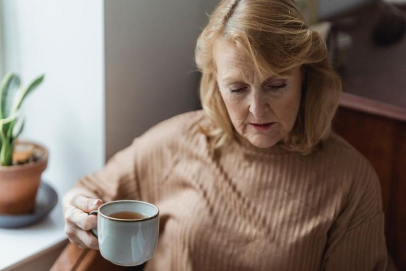 Mujer mayor descansando con una taza de té junto a la ventana