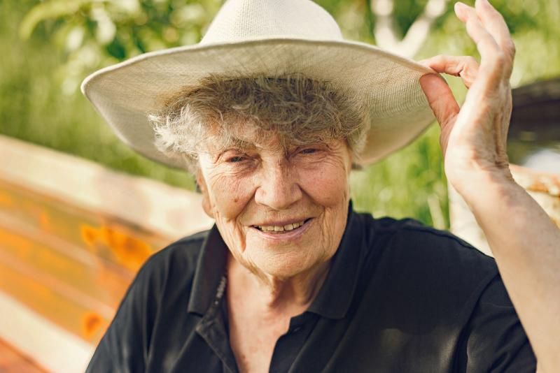Mujer mayor sonriendo al sol en un jardín con un sombrero de paja