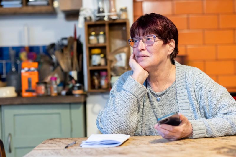 Mujer mayor pensativa con documentos y el móvil en la mesa de la cocina