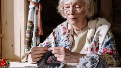 Mujer mayor tejiendo junto a una ventana soleada