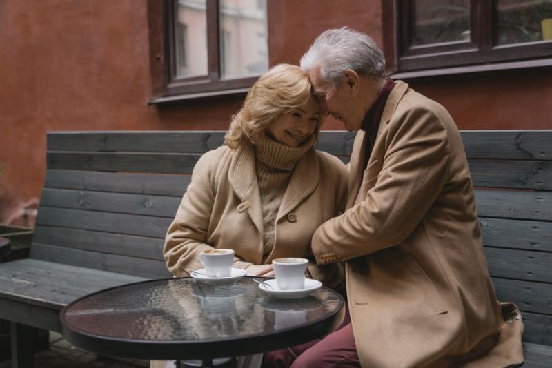 Pareja mayor tomando café y conversando en un banco