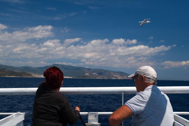 Pareja de personas mayores en la cubierta de un ferry mirando el mar y la costa