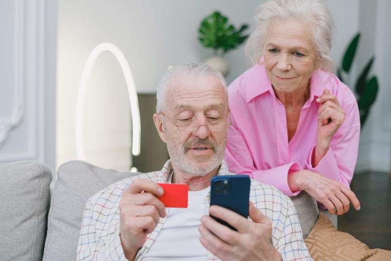 Pareja de personas mayores mirando el móvil y una tarjeta bancaria en casa