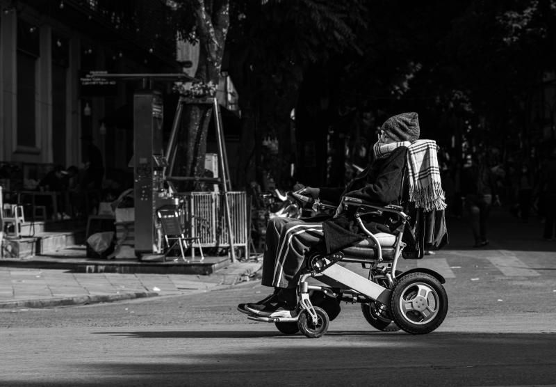 Persona mayor en silla de ruedas eléctrica por una calle de ciudad