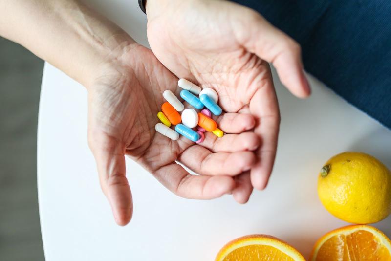 Manos sosteniendo varios suplementos y vitaminas de colores junto a una naranja
