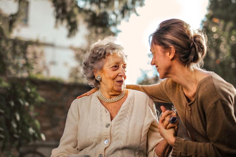 Hija mayor y su madre sonriendo cogidas de la mano en el jardín de casa