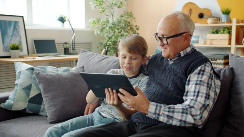 Abuelo y nieto sentados en el sofá mirando fotos en una tablet