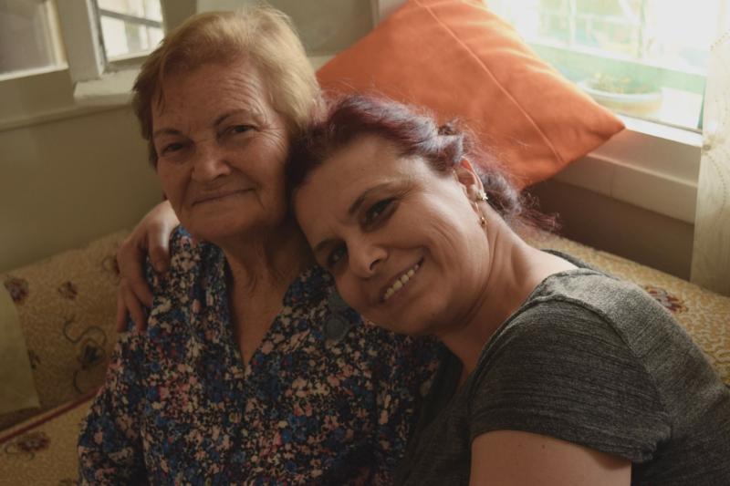 Mujer mayor sonriendo junto a la mujer que la cuida en el sofá de casa